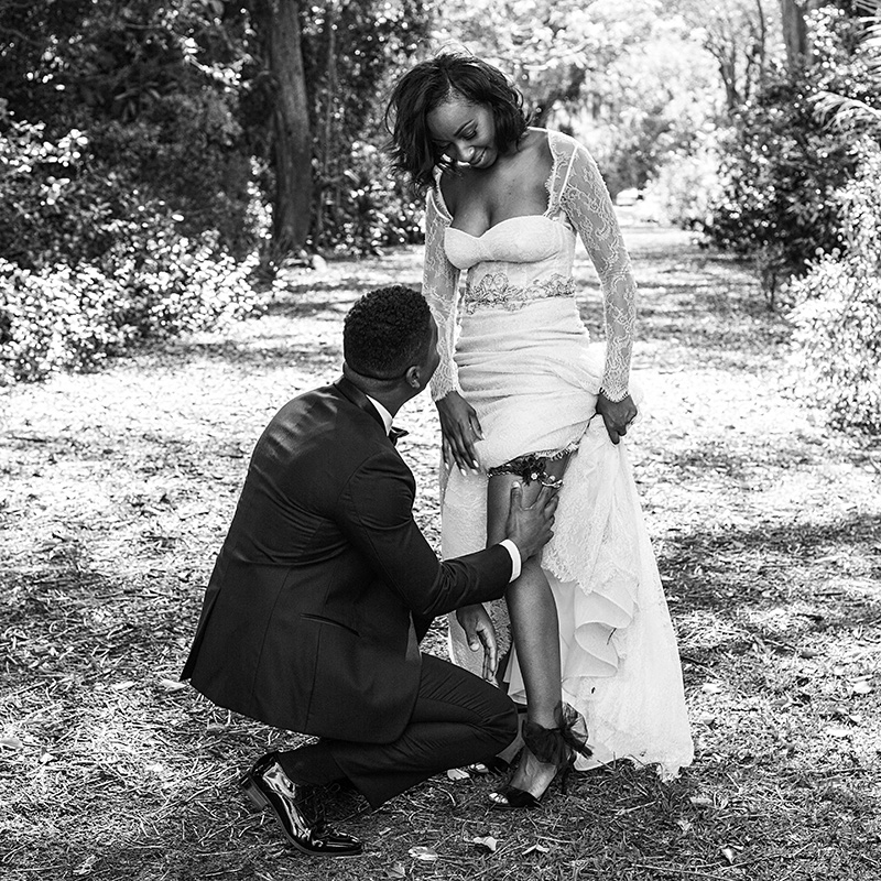 Timeless black-and-white shot of a groom assisting his bride with her garter at Fairchild Tropical Botanic Garden.