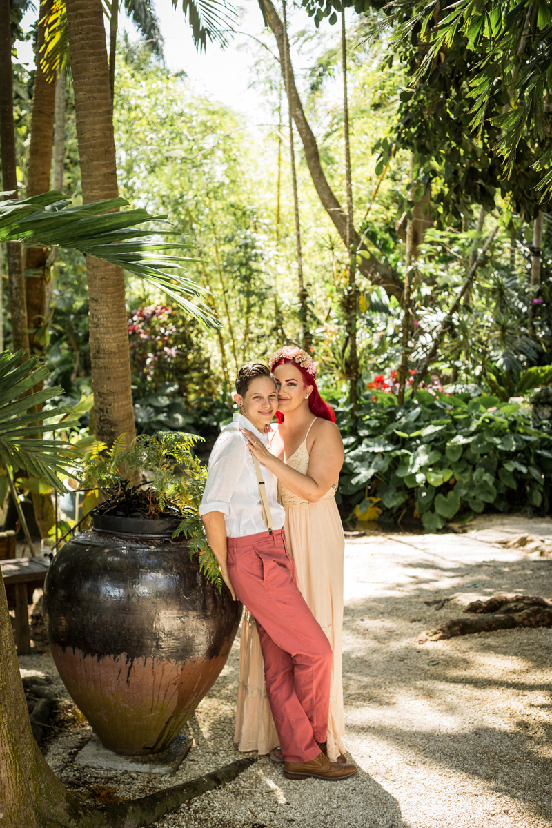 Bride and bride share an intimate moment atop a flower vase, surrounded by lush tropical beauty at Walton House