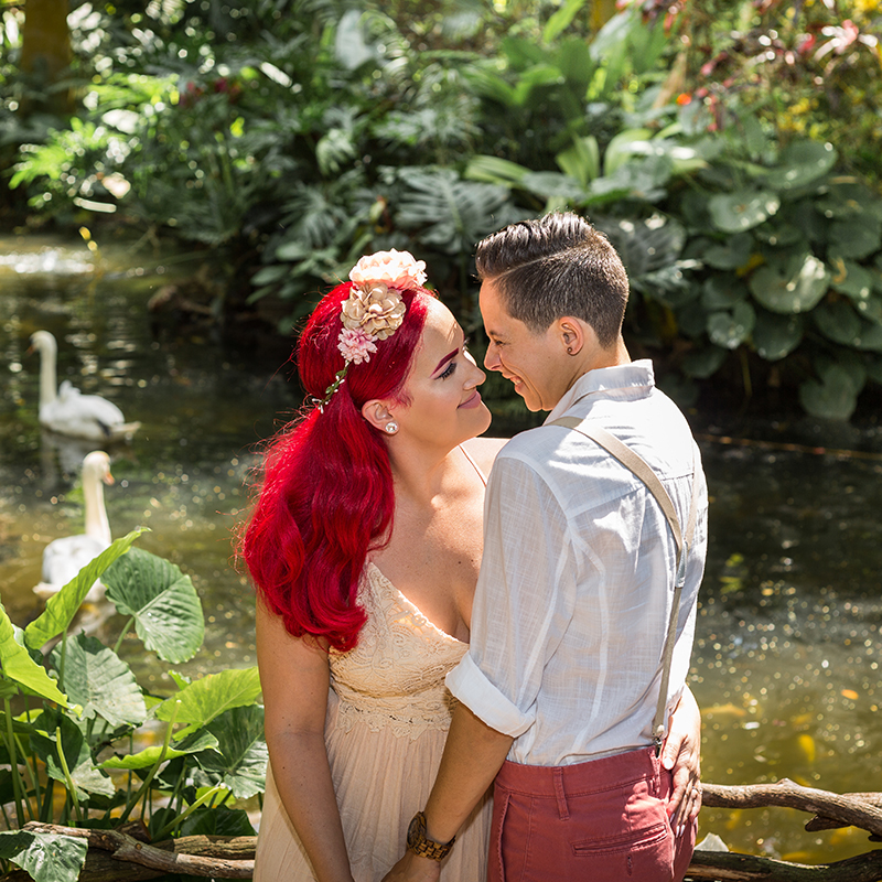 Bride and bride lock eyes in a tender embrace as swans drift by at The Historic Walton House in Homestead, FL.