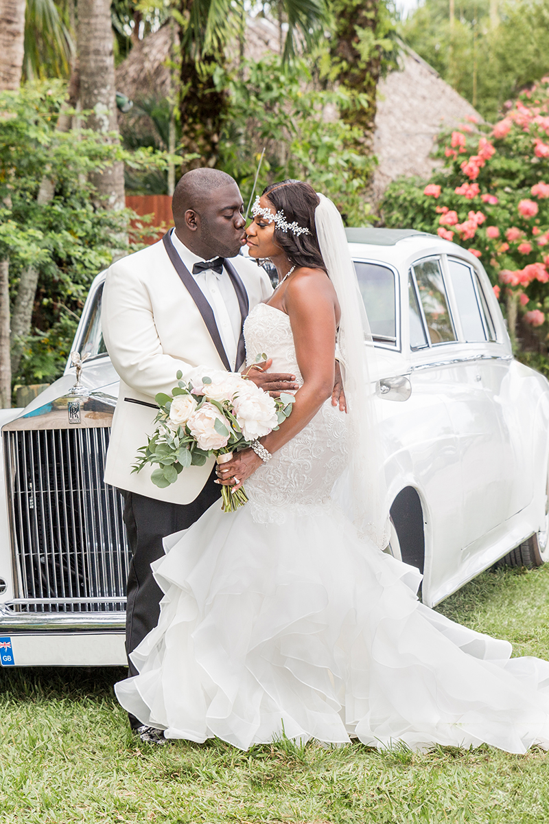 Groom kisses his bride as she holds her bouquet in front of a vintage Rolls Royce at The Bamboo Gallery, Davie.