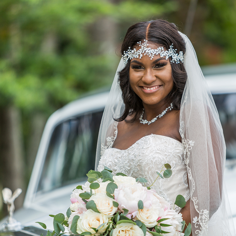 Radiant bride poses with her bouquet, smiling in front of a Rolls Royce at The Bamboo Gallery in South Florida.